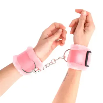 Γυναικείοι καρποί δεμένοι με ροζ χνουδωτές χειροπέδες KINK και μεταλλική αλυσίδα.
